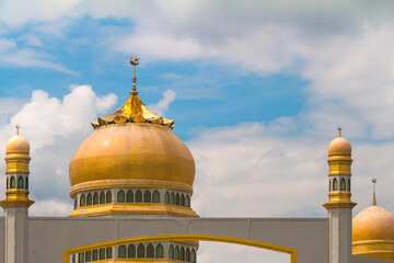 Ancient traditional golden mosque dome against white clouds on blue sky background in south Thailand