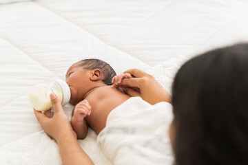 Mother or nurse feeding newborn baby with milk bottle. Newborn born sleeping and eating milk from...