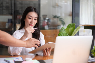 Portrait of young beautiful asian woman holding stylus pen, thinking and looking outside while...