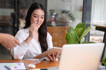 Portrait of young beautiful asian woman holding stylus pen, thinking and looking outside while...