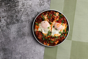 Shakshuka - eggs poached in spicy tomato pepper sauce on a round plate on a dark background. Top view, flat lay
