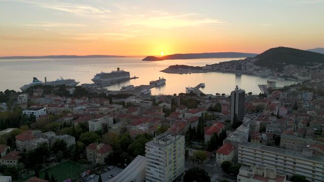 Split, Croatia - Aerial drone video of sunset over city with ships in the harbor zooming out