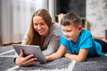 Happy loving family. Young mother and her son using tablet lying on carpet