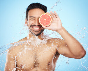 Face, water and grapefruit with a man model in studio on a blue background for hygiene or natural...