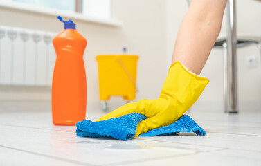 cleaning service. Woman wearing gloves cleaning floor. cleaning and care product for laminate and flooring. large orange bottle of laminate floor cleaner.