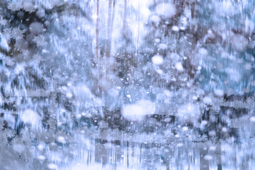 Winter landscape through a frozen window. Blurred snow background. Trees and plants covered with snow.