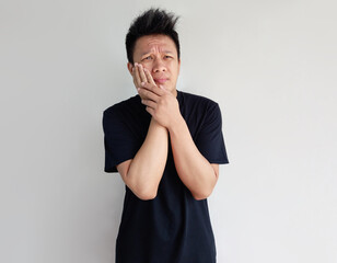 Young man posing having toothache with both hands on cheeks isolated on plain background