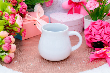 White blank creamer mug on the top of a small rounded table cloth surrounded by valentine themed...