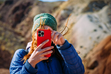 Woman traveller holding smartphone covering her face on blurred mountain background. Happy female...