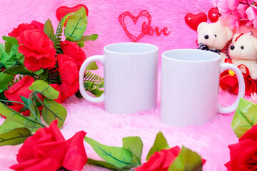 Two white blank coffee mug on the top of a fluffy pink carpet surrounded by valentine themed decorations