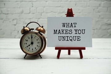 What makes you unique?  text and alarm clock on white brick wall and wooden background