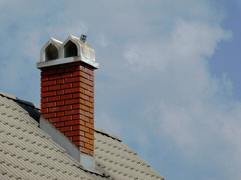 Brick Chimney Concrete Capping. Ornamental White Concrete Capstone. Gray Concrete Roof Tiles. Metal Flashing. Blue Sky. Bright Sunlight. Construction Concept. Modern Building Materials Concept.