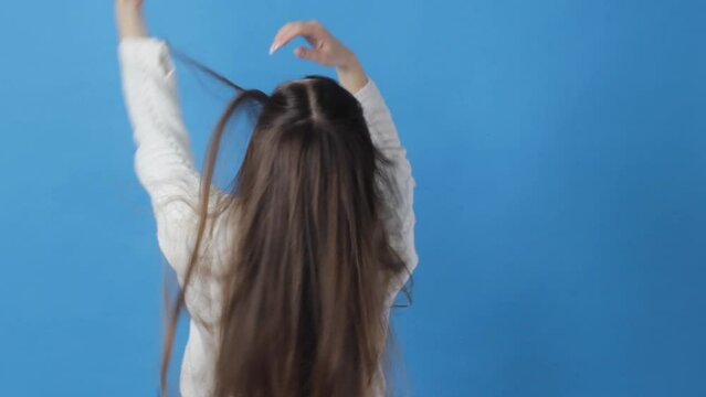 brunette girl straightens her long hair back view on a blue background.