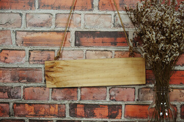Empty space of Wooden sign hanging with rope and dried flower decoration on brick wall background