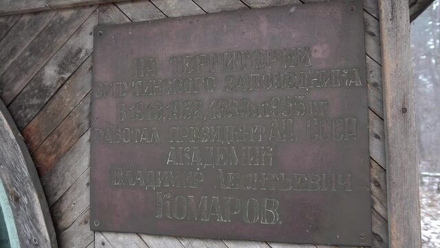 Commemorative plaque with the name of Academician Komarov on an old wooden house in the forest.