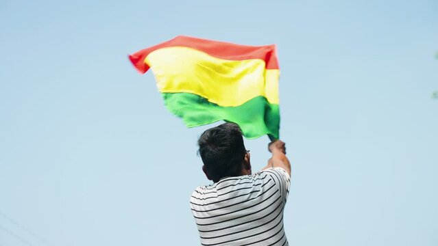 Back view shot of man waving black history month flag against sky - concept of freedom, independence and celebration
