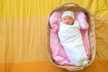 Newborn baby in a wrap on white blanket lay in a basket, Top view of newborn baby, Baby girl first day, Copy space, Sleeping baby concept.