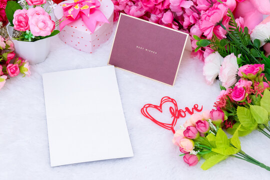 White blank greeting card paper on the top of a fluffy white carpet surrounded by valentine themed decorations