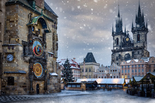 Winter view to the astronomical clock and the old town square of Prague with Tyn Church in the background and snow falling, Czech Republic