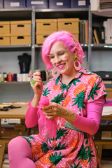 Dressmaker with pink hair and colorfull clothes hand sewing a piece of fabric in a sewing workshop.