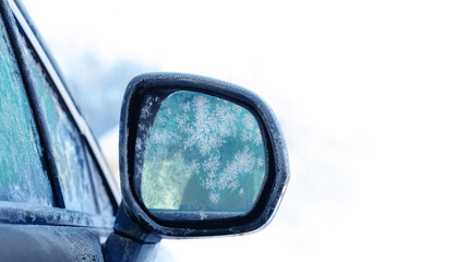 car mirror in frost close up, abstract light background. Black car with side mirror and windows in ice, snow. frozen cold weather, winter season. 