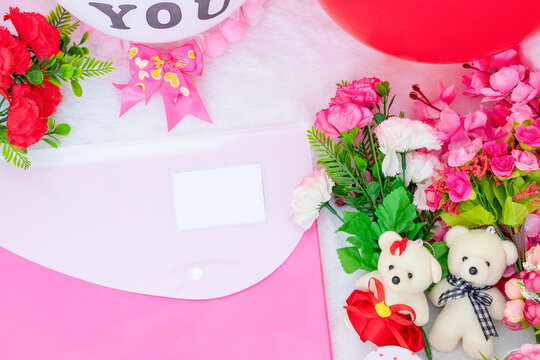 White blank business card paper on the corner of a pink envelope surrounded by valentine themed decorations