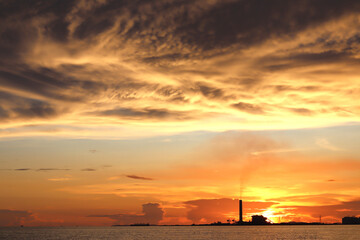 pollution released from the factory. industry site located beside the sea and the sunset in the evening. concept of the tower crane and construction site. there are much of pollution in the air.