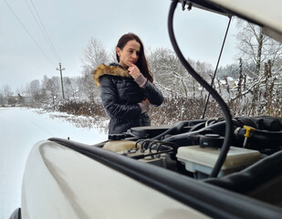 Female driver opened hood of car and looks at breakdown in winter on track