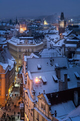 View of Prague roofs from the astronomical clock tower on the Old town Square with Powder tower in the background at night in winter. Snow. Prague. Christmas.