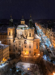 View of Prague roofs from the astronomical clock tower on the Old town Square with St. Nicolas Cathedral in the foreground at night in winter. Snow. Prague. Christmas.