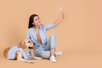 Happy woman taking selfie with cute Labrador Retriever on beige background. Space for text