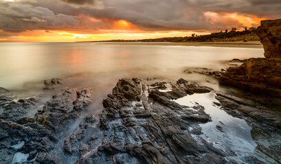 view of La Pelosa beach in Sardinia at sunrise with rocky reef in the foreground