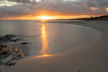 Fototapeta na wymiar La Pelosa beach in Sardinia at sunrise with a sunburst and rocks in the foreground