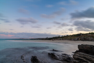 sunset over the picturesque white sand beach and turquoise waters at La Pelosa Beach with rocks in the foreground