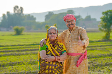 senior indian farmer couple showing thumps up at agriculture field