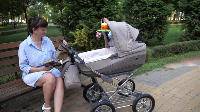 Mom with a stroller breathes fresh air in the park. A woman is reading a book. 4K Slow Mo