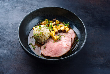 Traditioneller deutscher Schweinebraten mit Semmelknödel und Baby Kräuterseitlinge in dunkler Biersauce serviert als close-up in einer Nordic Design Schale mit Textfreiraum