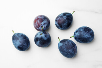 Fototapeta na wymiar Tasty ripe plums on white marble table, flat lay