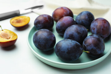 Plate with tasty ripe plums on white table, closeup