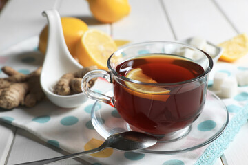 Cup of delicious ginger tea, sugar cubes and lemons on white wooden table, closeup