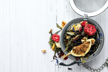 Snap infuser with dried herbal tea leaves and fruits on white wooden table, top view. Space for text