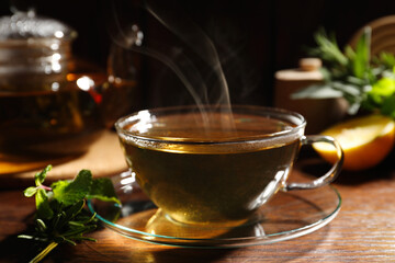Cup of aromatic herbal tea, mint and rosemary on wooden table