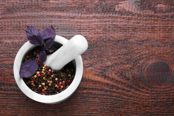 Mortar with peppercorns and basil on wooden table, top view. Space for text