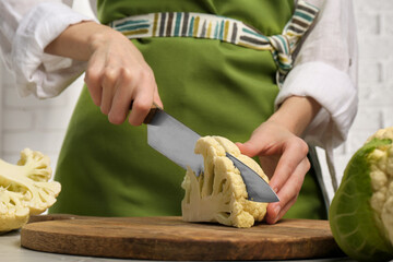 Woman cutting fresh cauliflower on wooden board, closeup