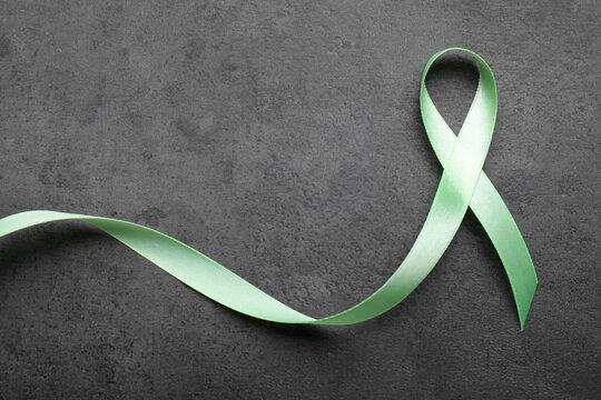 World Mental Health Day. Green ribbon on black background, top view with space for text