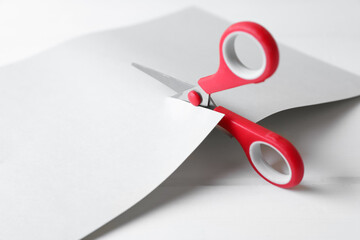 Red scissors cutting paper on white wooden background, closeup - obrazy, fototapety, plakaty