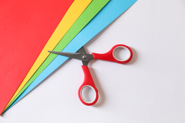 Red scissors and color sheets of paper on white background, flat lay