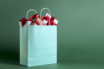 Turquoise paper shopping bag full of gift boxes on green background. Space for text