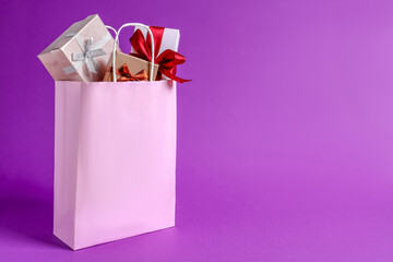 Pink paper shopping bag full of gift boxes on purple background. Space for text