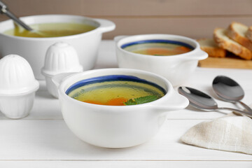 Delicious chicken bouillon with carrot and parsley on white wooden table, closeup
